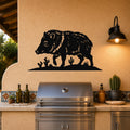 Black metal javelina wall art with cactus cutouts, mounted on a stucco wall above a stainless steel grill in an outdoor kitchen.