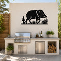 Black metal javelina wall art with cactus and agave cutouts, mounted on a beige outdoor wall above a kitchen counter.