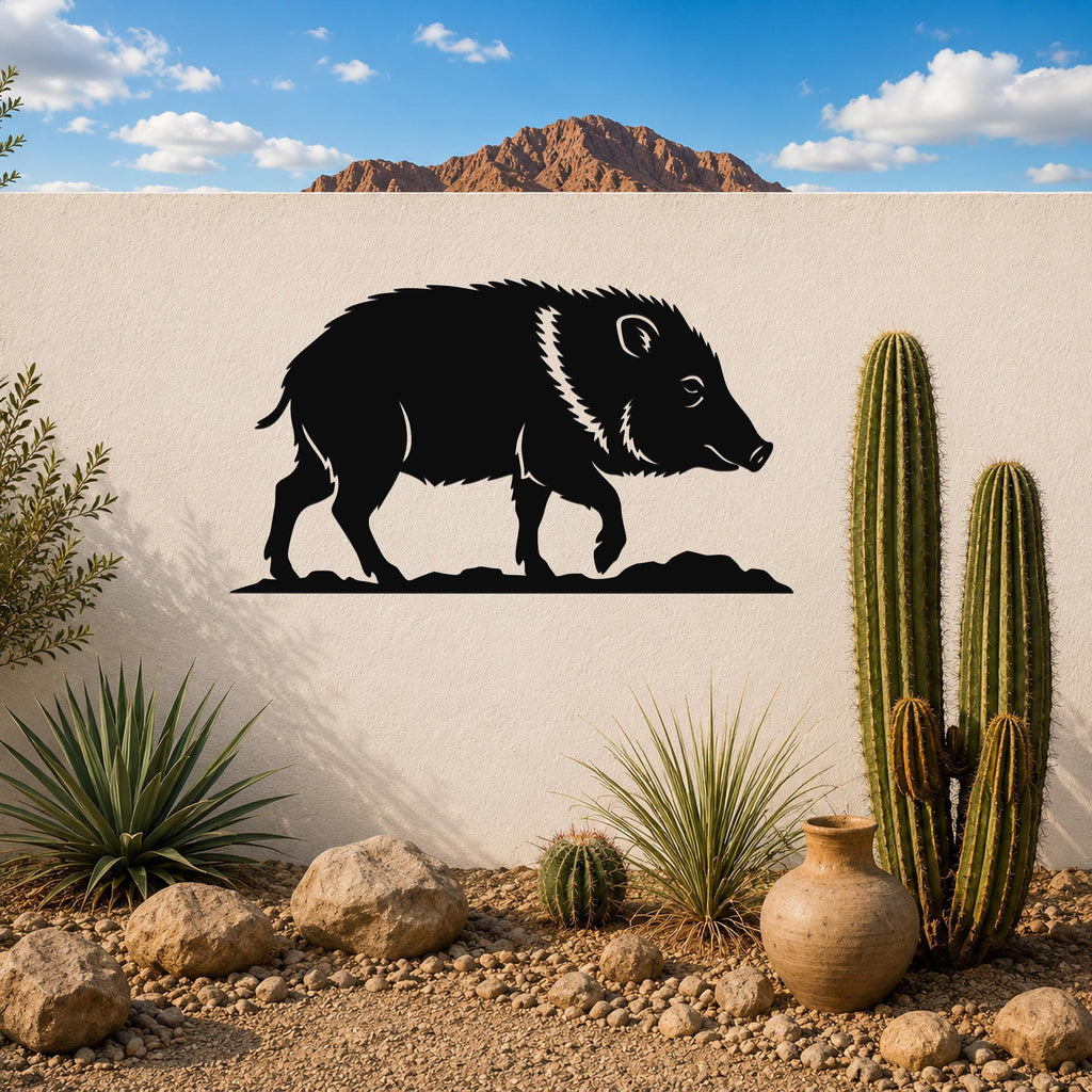Black metal javelina wall art silhouette with white facial and neck details, mounted on a white outdoor wall above a desert garden with cacti and rocks.