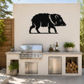 Black metal javelina wall art silhouette with internal cutout details, mounted on an outdoor patio wall above a stainless steel grill and countertop.