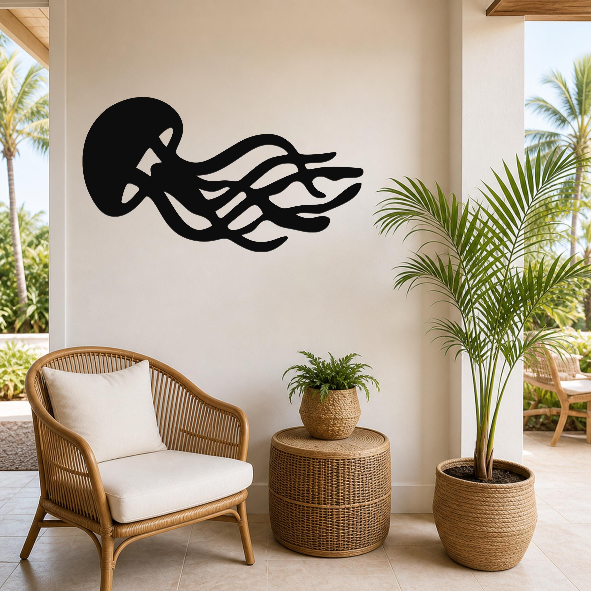 Black metal jellyfish wall art with flowing tentacle cutouts, mounted on a light-colored wall above a wicker chair in a tropical patio setting.