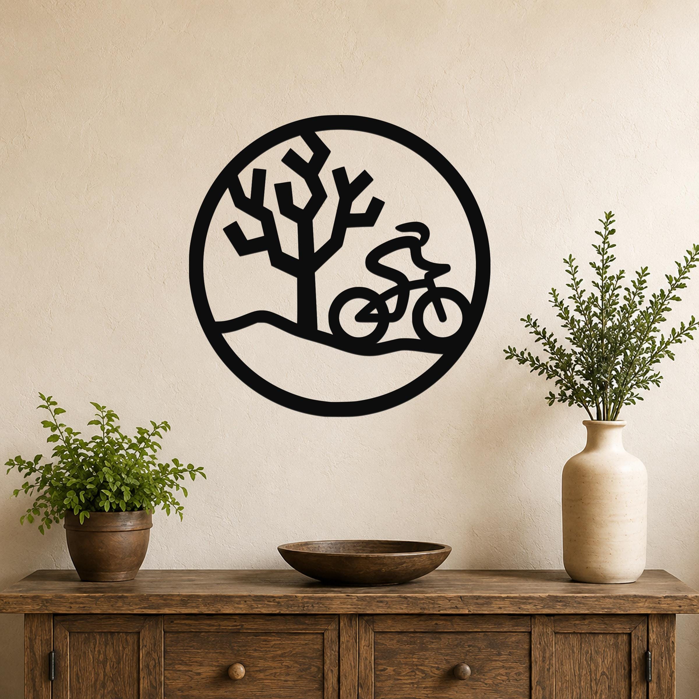 Black metal wall art with a circular silhouette of a cyclist and a Joshua tree, mounted above a wooden console table in a living room.