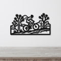 Black metal wall art cutout of a cyclist riding through a desert landscape with Joshua trees and cacti, mounted on a white wall above a wooden surface.