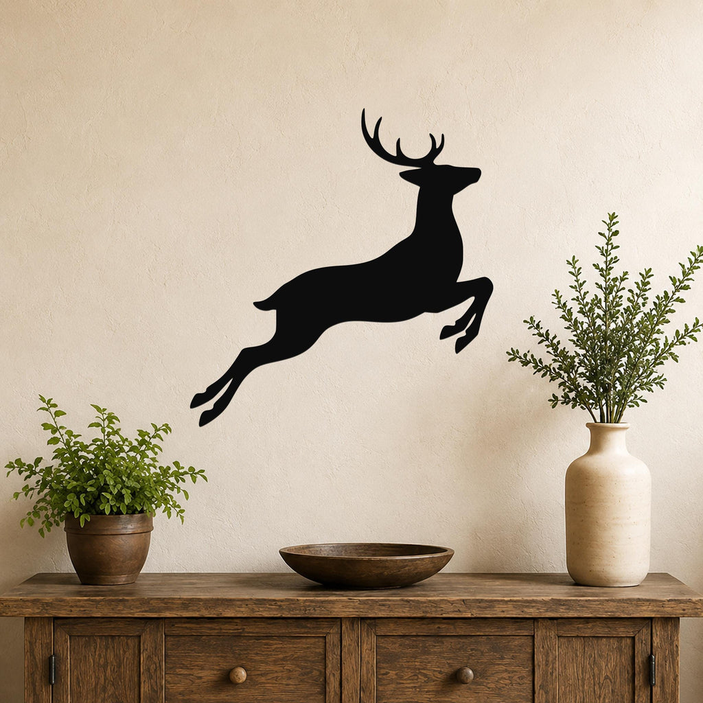 Black metal jumping deer wall art silhouette mounted above a wooden console table in a living room, flanked by two potted plants.