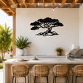 Black metal wall art of a wind-sculpted juniper tree silhouette, mounted on a white outdoor wall above a kitchen counter with wicker bar stools.