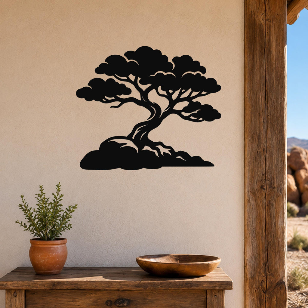 Black metal wall art cutout of a bonsai-style juniper tree with layered branches and roots, mounted on a beige wall above a wooden table in a rustic outdoor entryway.