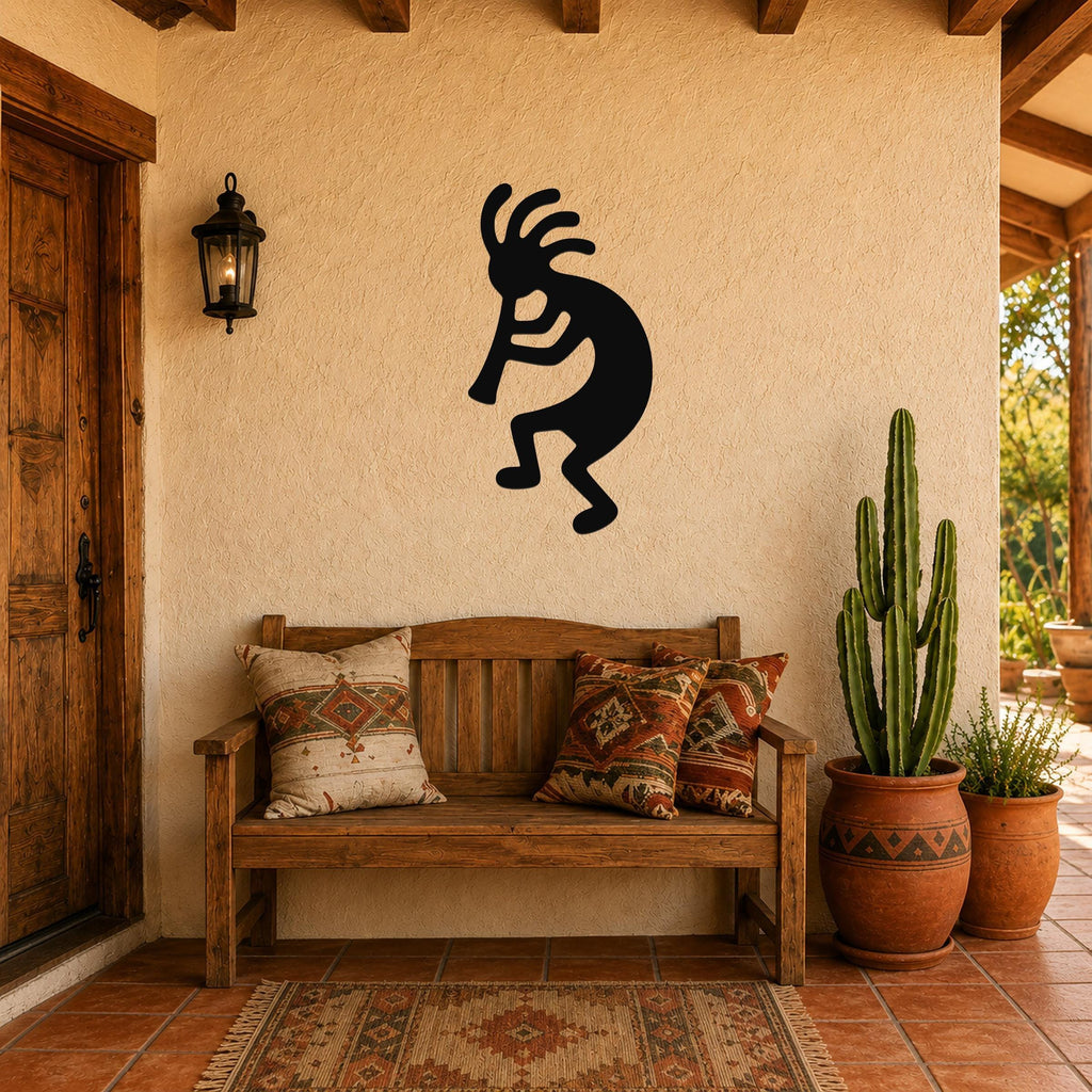 Black metal Kokopelli wall art silhouette with flute and feathered headdress, mounted on a stucco wall above a wooden bench in a patio entryway.