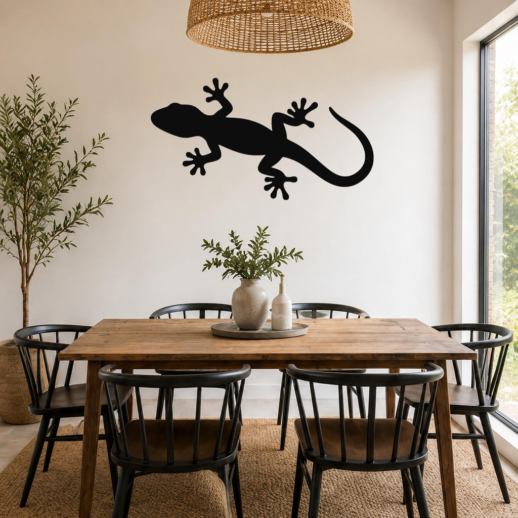 Black metal gecko wall art silhouette mounted on a white wall above a wooden dining table in a bright dining room.