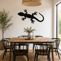 Black metal gecko wall art silhouette mounted on a white wall above a wooden dining table in a bright dining room.