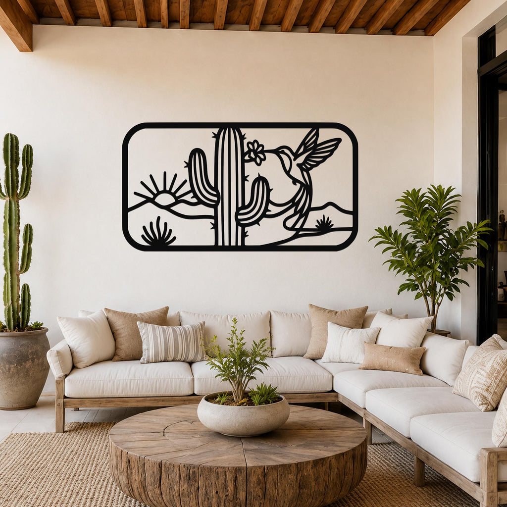 Black metal wall art with a desert scene of saguaro cactus, hummingbird, and sun cutouts, mounted above a white sofa in a living room.