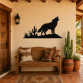 Black metal wall art silhouette of a coyote howling on a rock with cacti, mounted above a wooden bench on a stucco wall in a rustic patio setting.