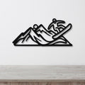 Black metal wall art featuring a snowboarder silhouette in motion over mountain peaks, mounted on a white wall above a wooden surface.