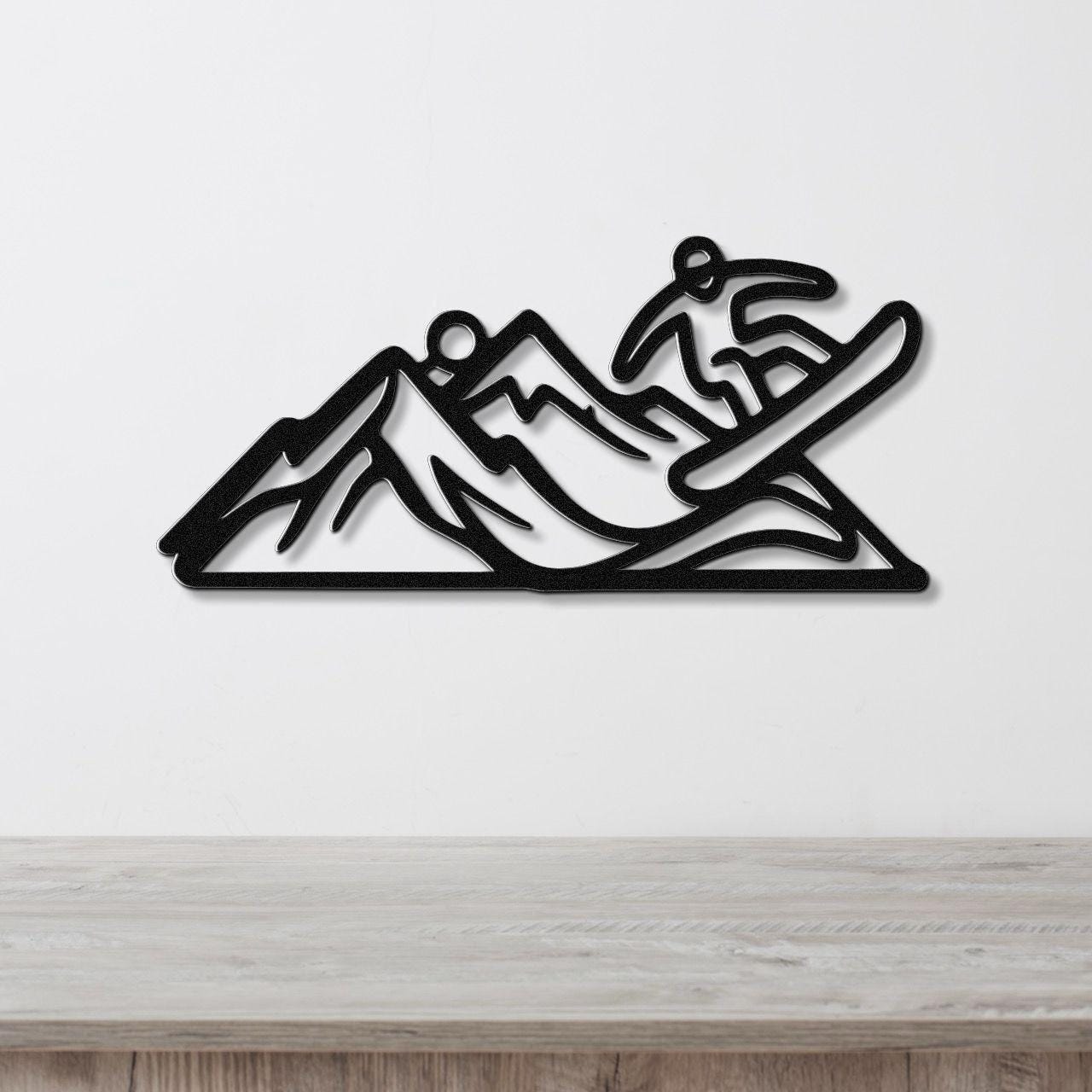 Black metal wall art featuring a snowboarder silhouette in motion over mountain peaks, mounted on a white wall above a wooden surface.
