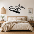 Black metal wall art silhouette of a snowboarder in motion, mounted above a bed in a neutral bedroom.