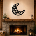 Black metal crescent moon wall art with intricate internal cutouts, mounted above a stone fireplace in a rustic living room.