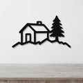 Black metal wall art cutout of a cabin and pine tree silhouette, mounted on a white wall above a light wood counter.
