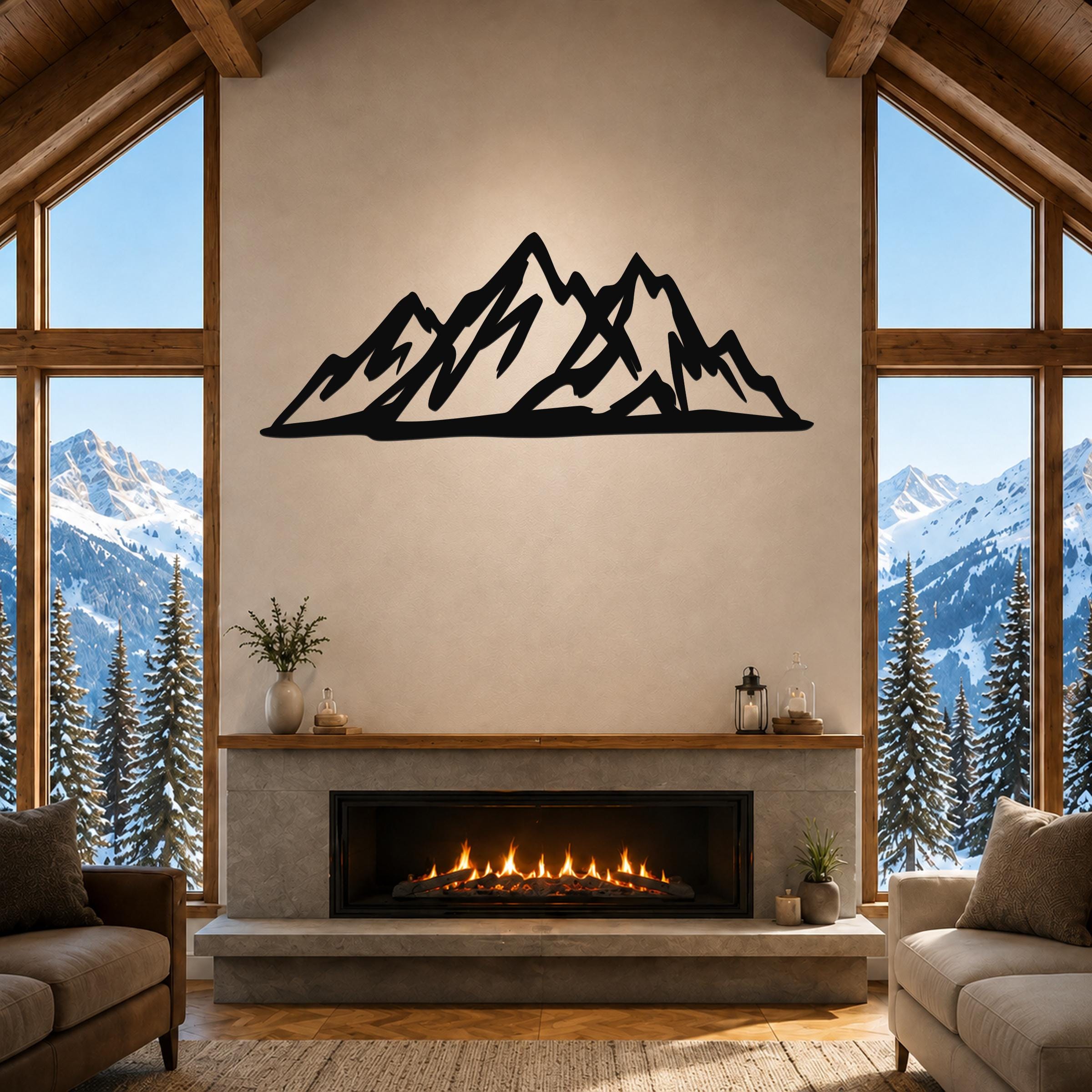 Black metal mountain silhouette wall art mounted above a fireplace in a rustic living room with large windows overlooking snowy peaks.