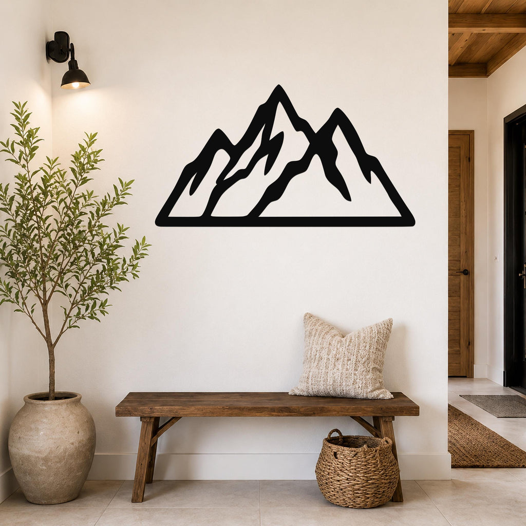 Black metal mountain silhouette wall art with layered peaks, mounted on a white wall above a wooden bench in a rustic entryway.