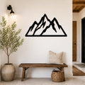 Black metal mountain silhouette wall art with layered peaks, mounted on a white wall above a wooden bench in a rustic entryway.