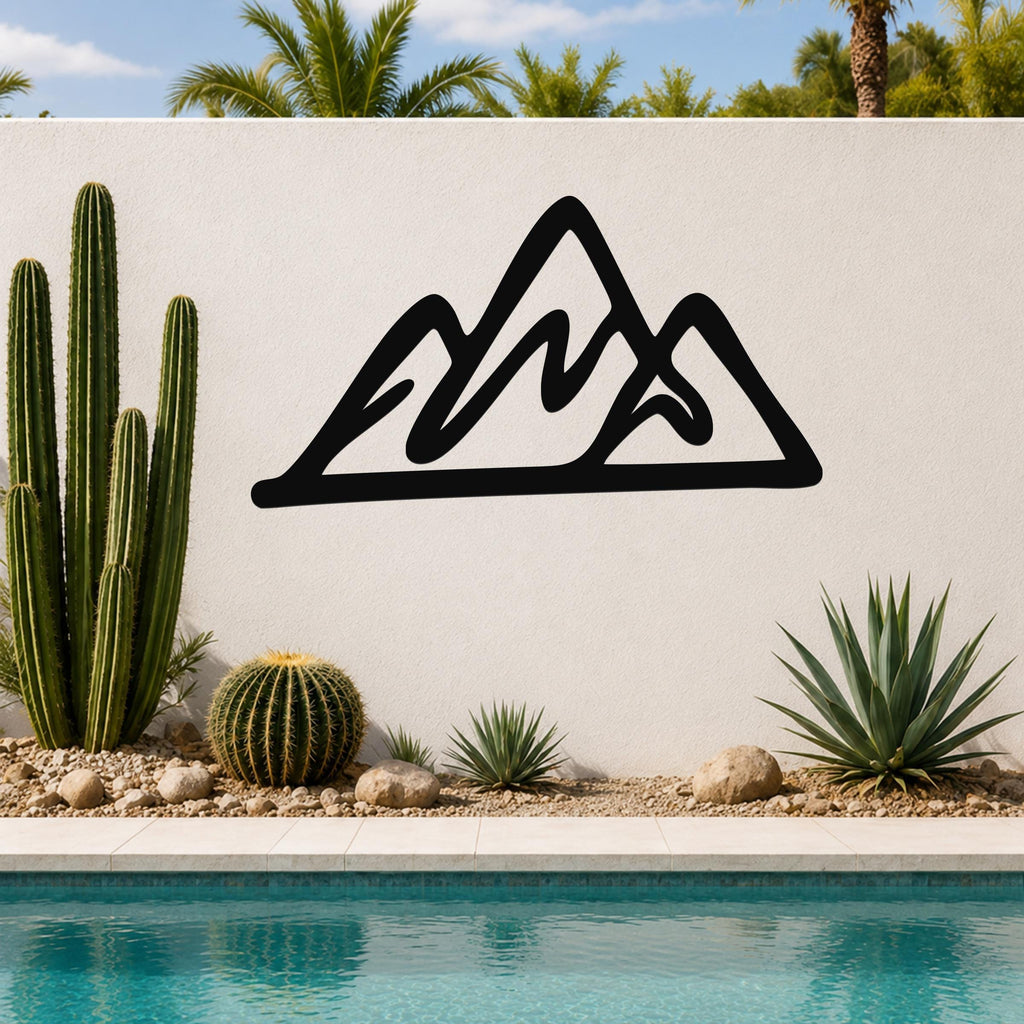 Black metal mountain silhouette wall art with layered peaks, mounted on a white outdoor wall above a pool with cacti and palm trees in the background.