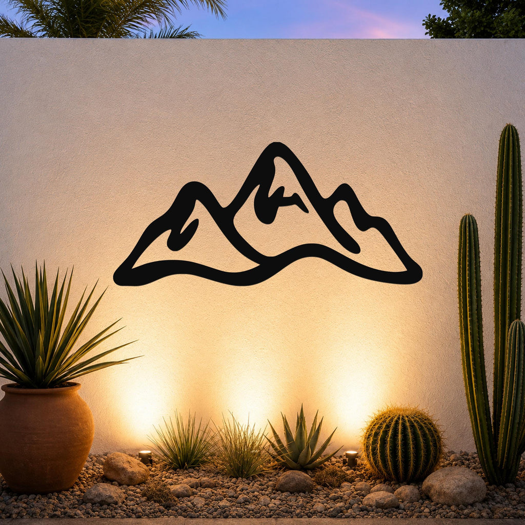 Black metal mountain range wall art with a silhouette design, mounted on an outdoor wall above a desert garden with cacti and warm ground lighting.