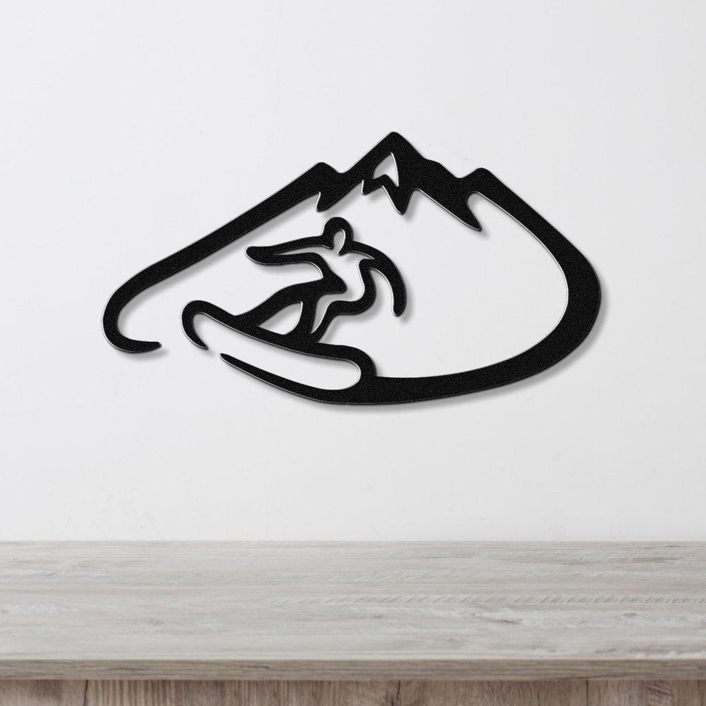 Black metal wall art featuring a snowboarder silhouette inside a mountain outline, mounted on a white wall above a wooden surface.