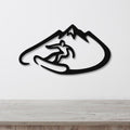 Black metal wall art featuring a snowboarder silhouette inside a mountain outline, mounted on a white wall above a wooden surface.