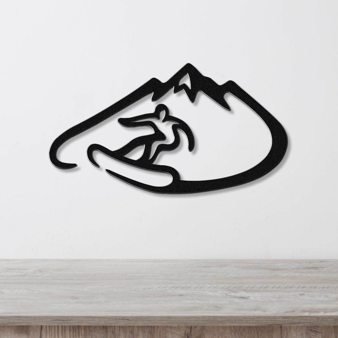Black metal wall art featuring a snowboarder silhouette inside a mountain outline, mounted on a white wall above a wooden surface.