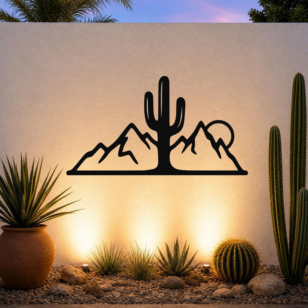 Black metal wall art with a saguaro cactus and mountain silhouette, mounted on an outdoor wall above a desert garden with potted plants and ground lights.