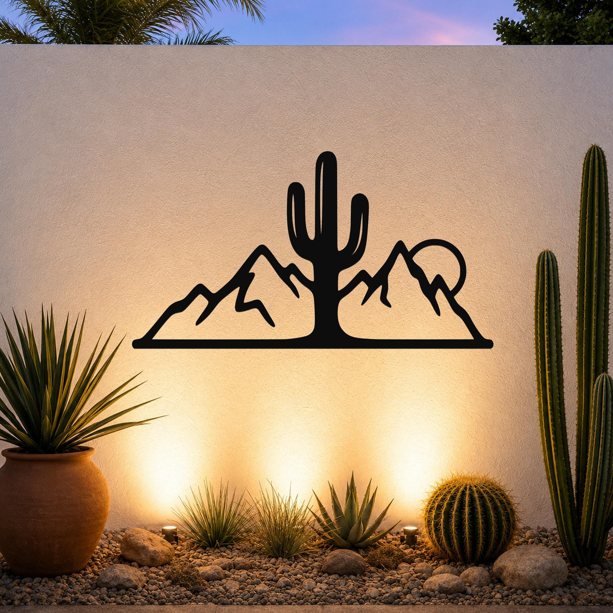 Black metal wall art with a saguaro cactus and mountain silhouette, mounted on an outdoor wall above a desert garden with potted plants and ground lights.