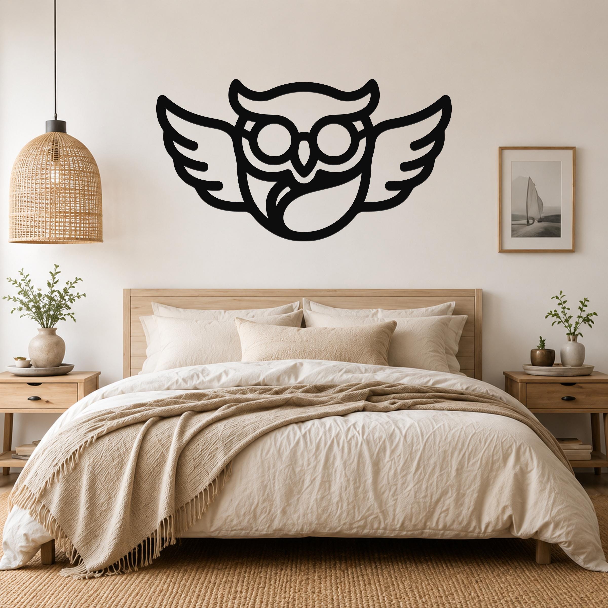 Black metal wall art silhouette of a bespectacled owl with spread wings, mounted above a bed in a neutral bedroom.