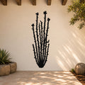 Black metal ocotillo wall art with spiny stems and flower cutouts, mounted on a light-colored outdoor wall above a tiled patio.