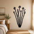 Black metal ocotillo wall art with flower and branch cutouts, mounted on a beige bedroom wall above a bed.