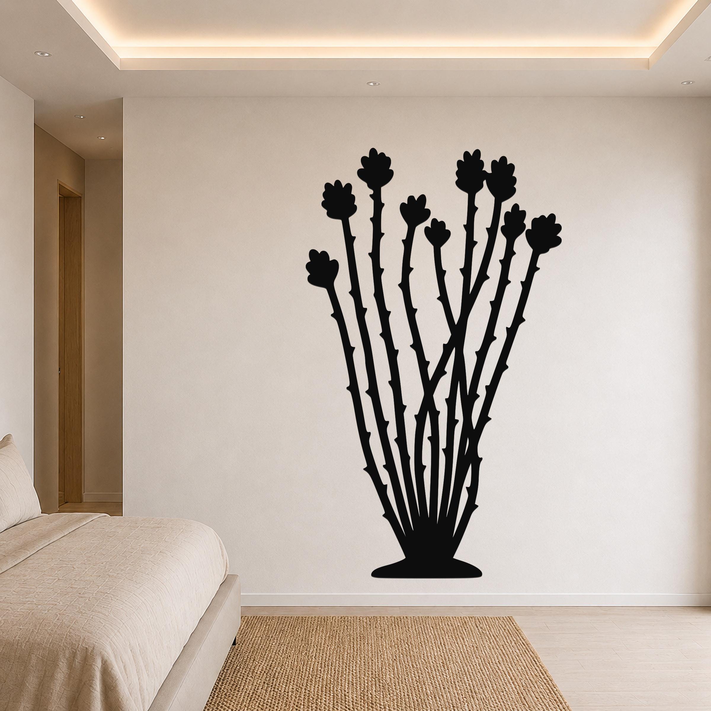 Black metal ocotillo wall art with flower and branch cutouts, mounted on a bedroom wall above a bed.