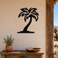 Black metal palm tree wall art with a silhouette design, mounted on a beige wall above a wooden table in a patio setting.