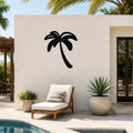 Black metal palm tree wall art silhouette mounted on a white outdoor wall beside a lounge chair and pool.