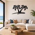 Black metal palm tree wall art with two silhouetted trees and a curved base, mounted above a white sofa in a living room with ocean views.