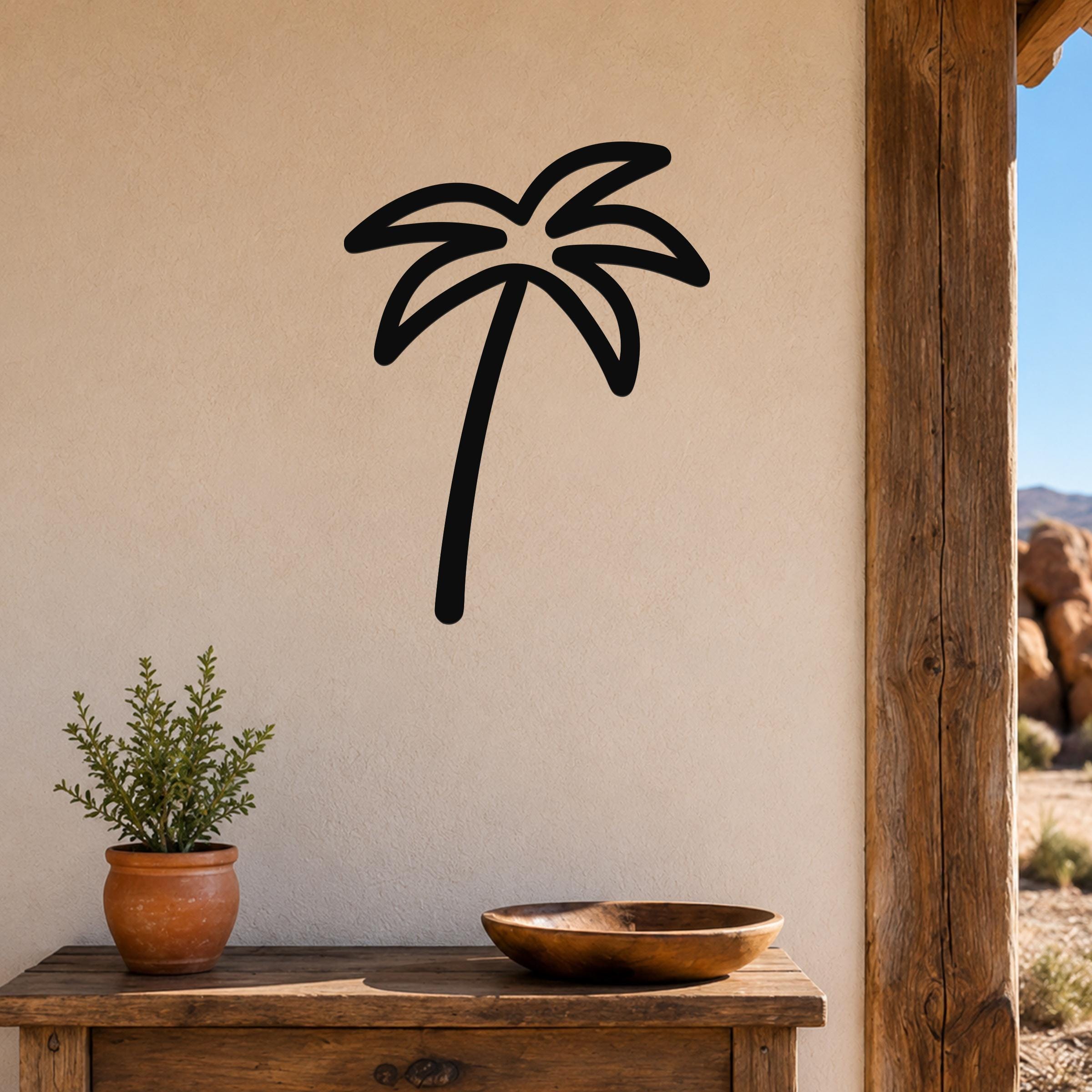 Black metal palm tree wall art with a silhouette design, mounted on a beige wall above a wooden table in a patio setting.