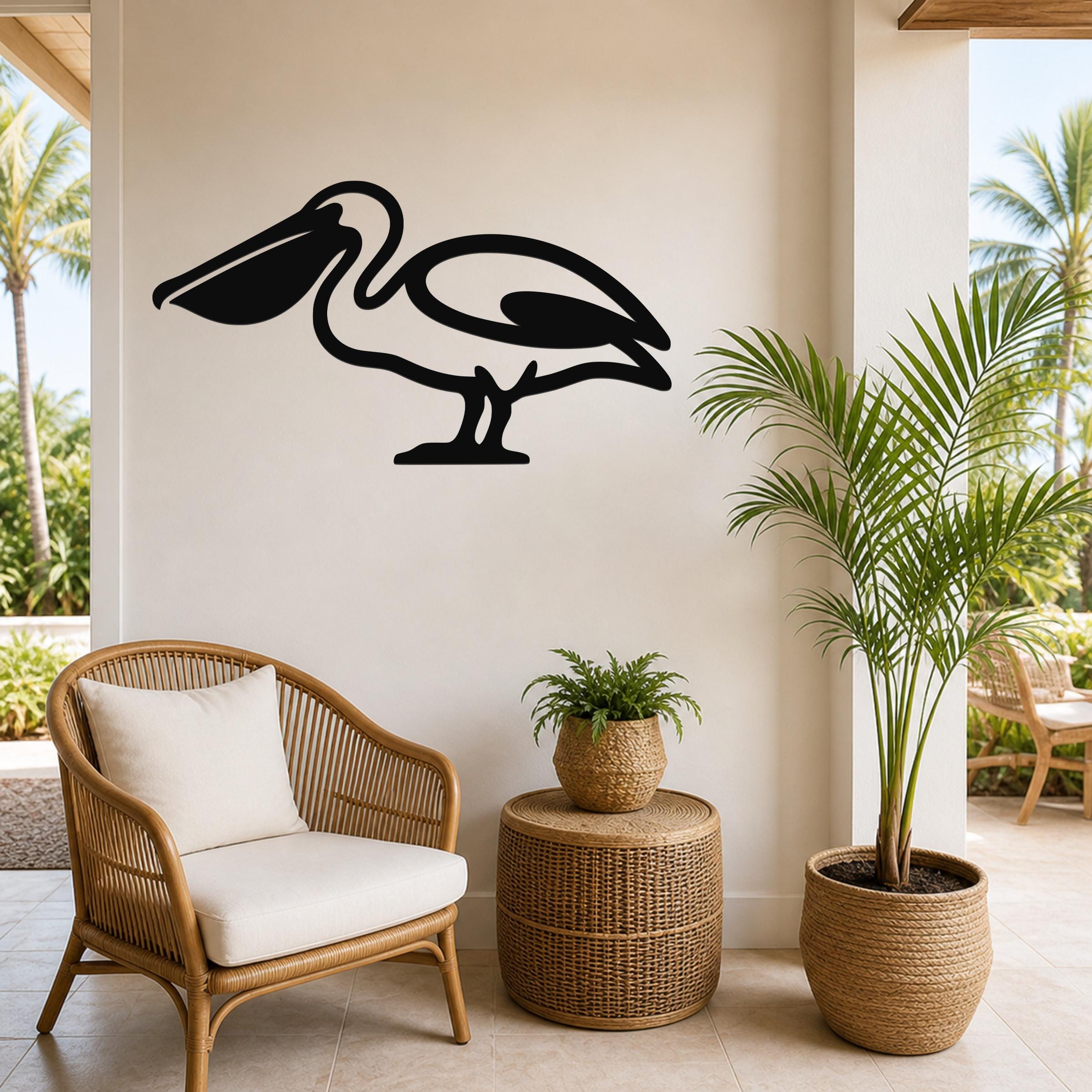 Black metal pelican wall art silhouette mounted on a beige wall above a wicker chair in a coastal patio setting.