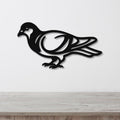 Black metal pigeon wall art with internal cutout details, mounted on a white wall above a light wood countertop.