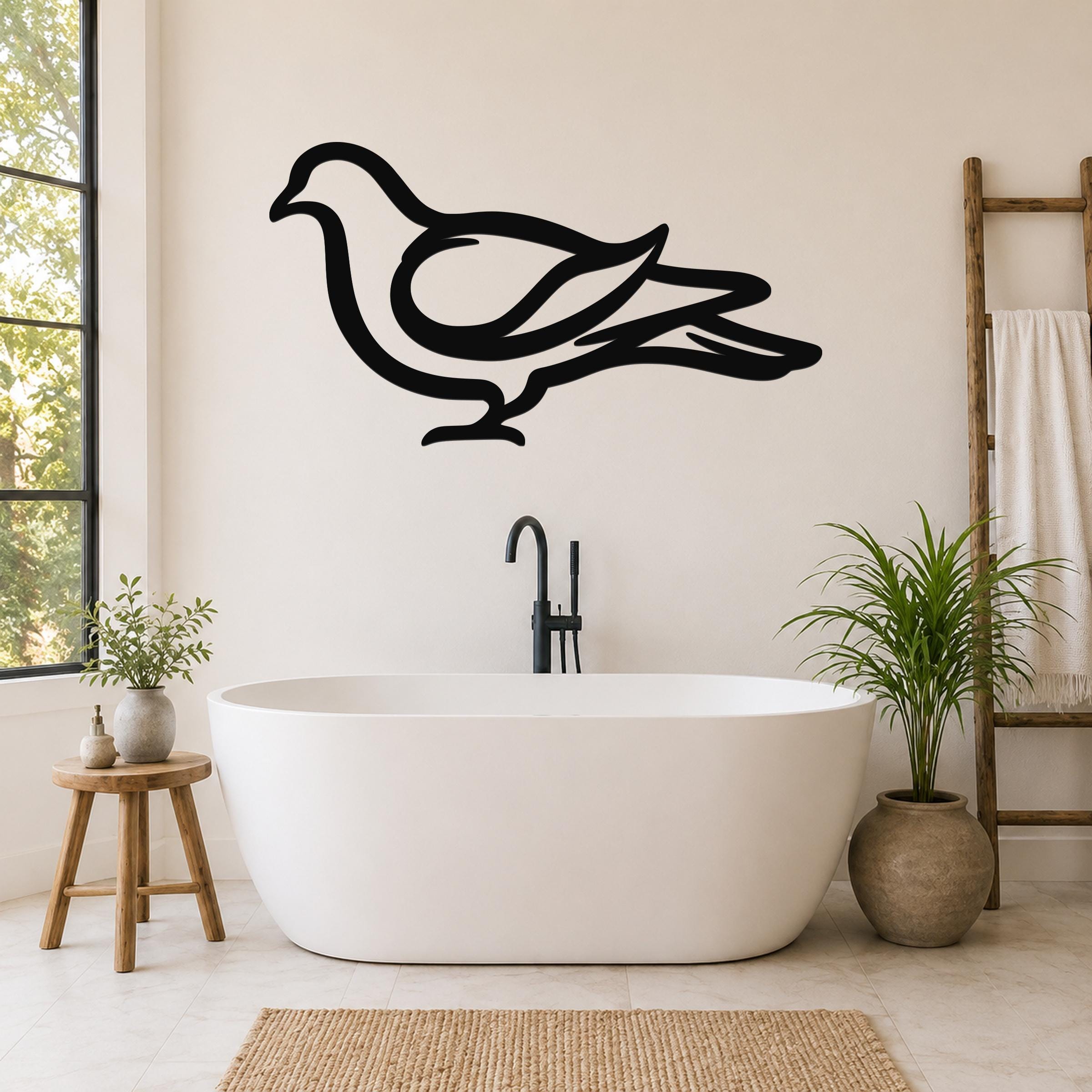 Black metal pigeon wall art silhouette mounted on a bathroom wall above a freestanding tub, with visible cutout details of the bird's wings and tail.