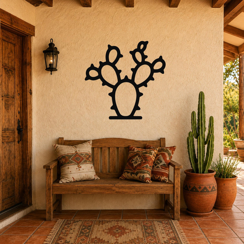 Black metal prickly pear cactus wall art with spiny silhouette cutouts, mounted on a stucco wall above a wooden bench in a rustic patio entryway.