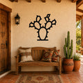 Black metal prickly pear cactus wall art with spiny silhouette cutouts, mounted on a stucco wall above a wooden bench in a rustic patio entryway.
