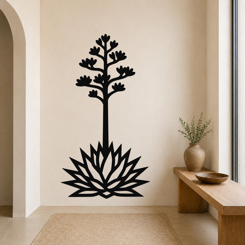 Black metal wall art in the silhouette of a blooming agave plant with a tall stem and spiky leaves, mounted on a beige wall above a woven rug in a minimalist entryway.