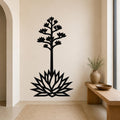 Black metal wall art in the silhouette of a blooming agave plant with a tall stem and spiky leaves, mounted on a beige wall above a woven rug in a minimalist entryway.