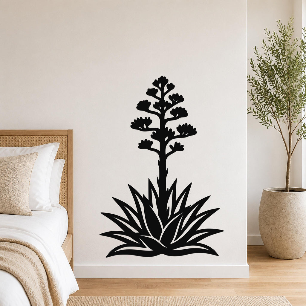 Black metal agave wall art with a blooming flower silhouette, mounted on a bedroom wall above a bed.