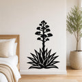 Black metal agave wall art with a blooming flower silhouette, mounted on a bedroom wall above a bed.