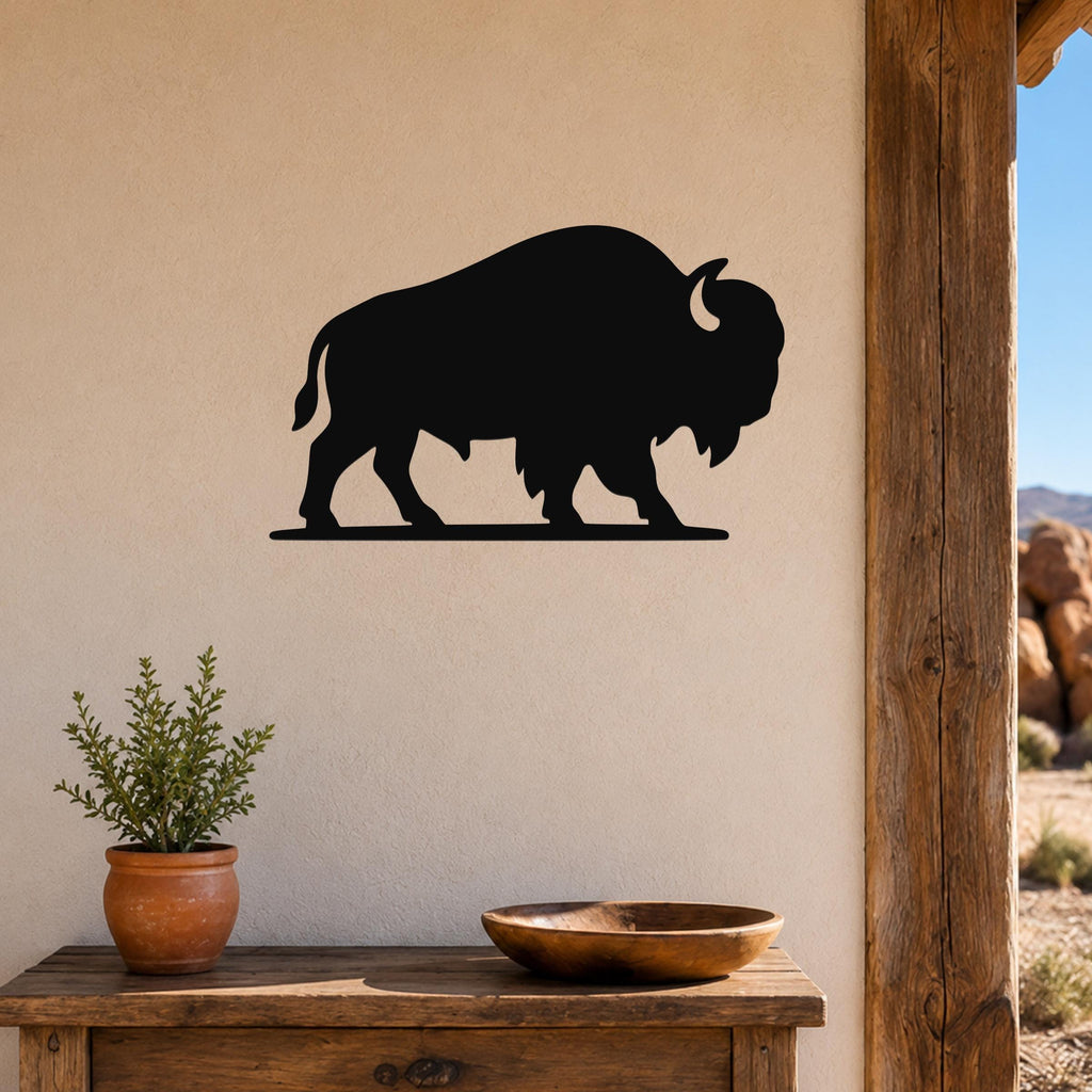 Black metal bison silhouette wall art mounted on a beige wall above a wooden table with a potted plant and wooden bowl.