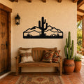 Black metal wall art silhouette of a saguaro cactus and desert mountains, mounted on a stucco wall above a wooden bench in a patio entryway.