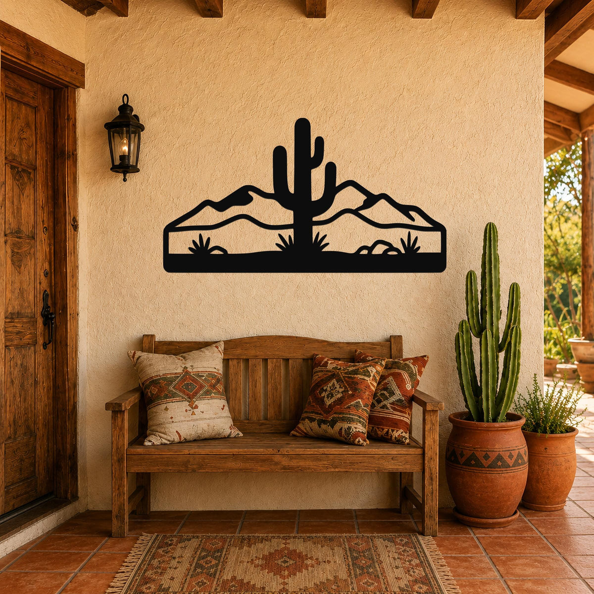 Black metal wall art silhouette of a saguaro cactus and desert mountains, mounted on a stucco wall above a wooden bench in a patio entryway.